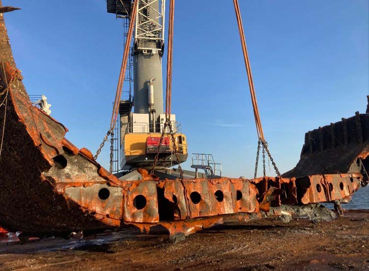 Rusted hull filled with holes is lowered to the ground